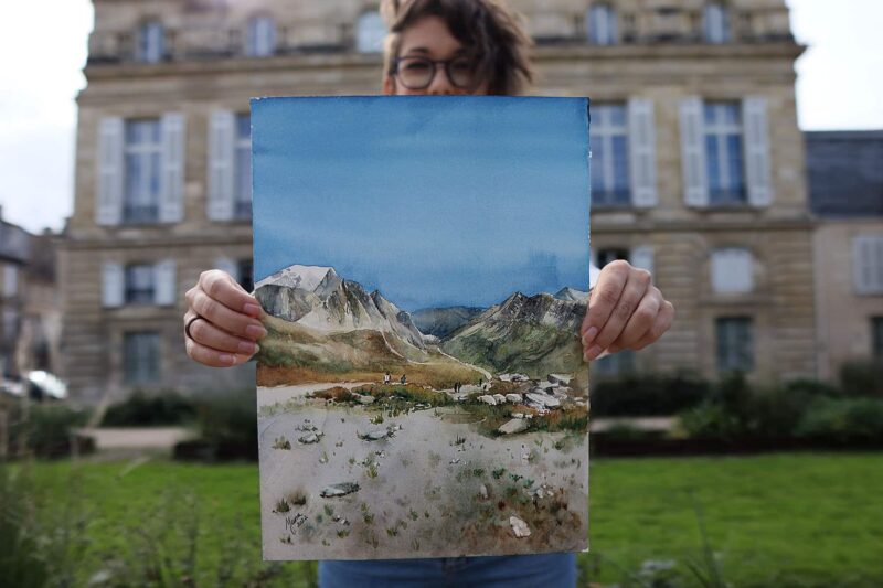 an artist holding a watercolor painting of mountain landscape