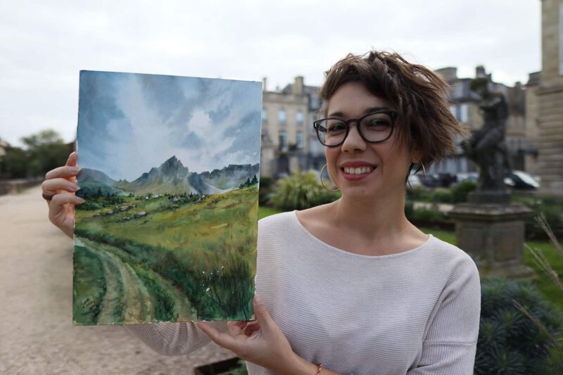 an artist holding a watercolor painting pf a green valley in the alps